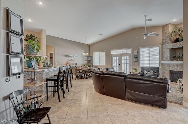 tiled living room featuring a stone fireplace, lofted ceiling, ceiling fan, and french doors