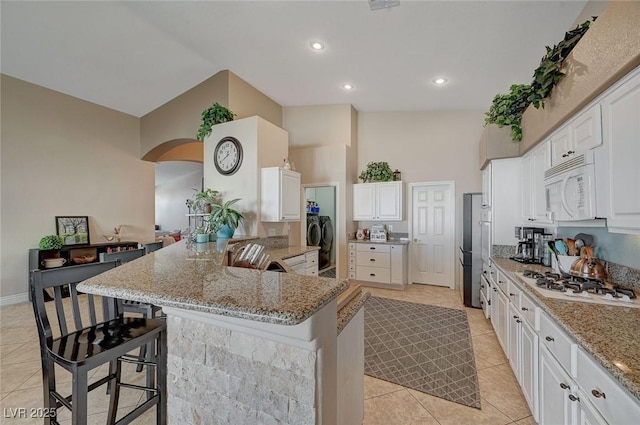 kitchen with a kitchen bar, white cabinetry, kitchen peninsula, white appliances, and light stone countertops