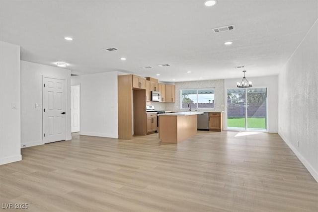 kitchen featuring appliances with stainless steel finishes, pendant lighting, light wood-type flooring, a center island, and an inviting chandelier