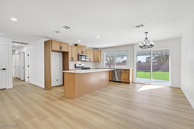 kitchen with pendant lighting, appliances with stainless steel finishes, tasteful backsplash, light hardwood / wood-style floors, and a kitchen island