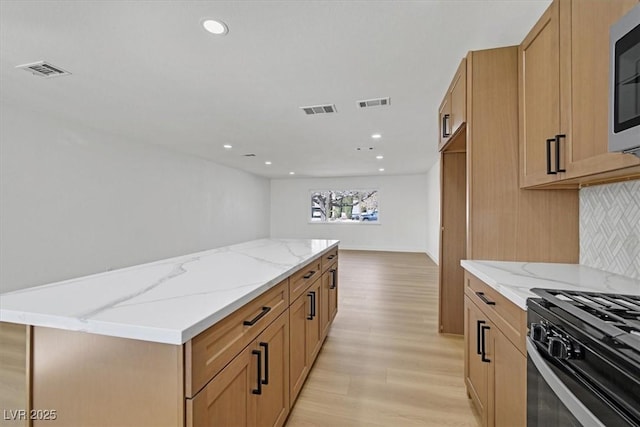 kitchen with light stone counters, decorative backsplash, light hardwood / wood-style floors, and a center island