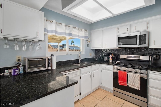 kitchen with appliances with stainless steel finishes, sink, white cabinets, decorative backsplash, and dark stone counters