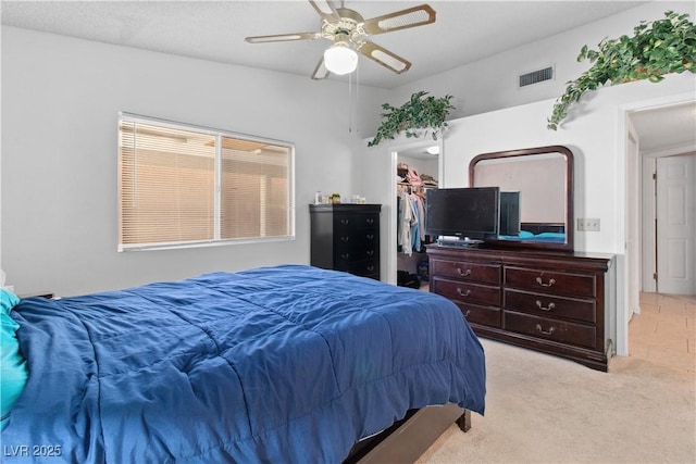 bedroom featuring a walk in closet, light colored carpet, and ceiling fan