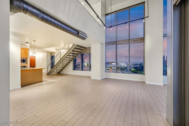 unfurnished living room with light wood-style floors, baseboards, a high ceiling, and stairs