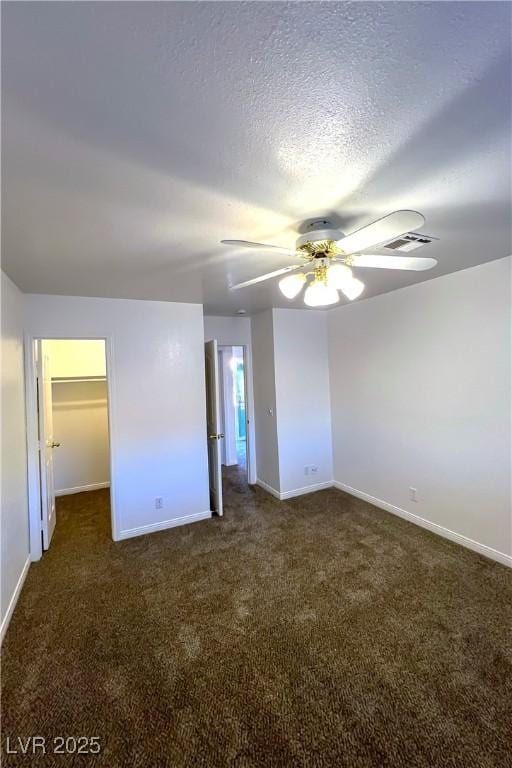 unfurnished bedroom with ceiling fan, a spacious closet, a textured ceiling, and dark colored carpet