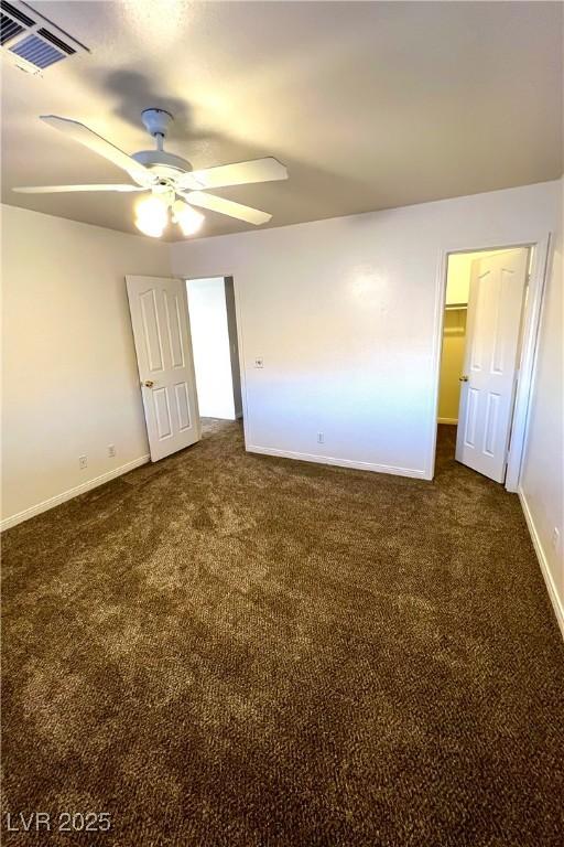 unfurnished bedroom featuring ceiling fan, a walk in closet, dark carpet, and a closet