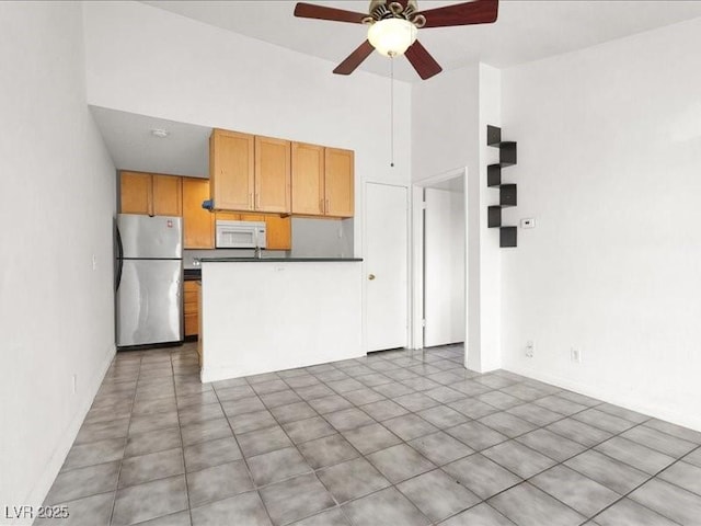 kitchen with dark countertops, ceiling fan, freestanding refrigerator, a peninsula, and white microwave