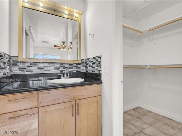 bathroom featuring tile patterned floors, vanity, a walk in closet, baseboards, and decorative backsplash