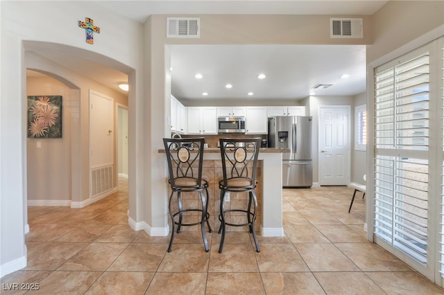 kitchen featuring light tile patterned floors, white cabinetry, stainless steel appliances, a kitchen bar, and kitchen peninsula