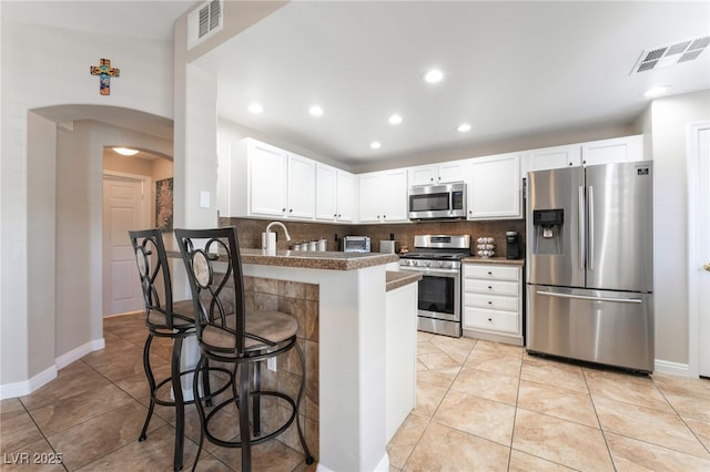 kitchen featuring appliances with stainless steel finishes, a breakfast bar, white cabinets, decorative backsplash, and kitchen peninsula