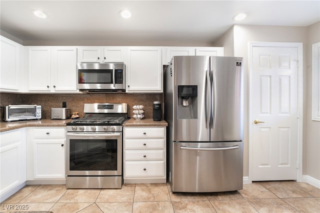 kitchen featuring appliances with stainless steel finishes, dark stone countertops, white cabinets, backsplash, and light tile patterned floors