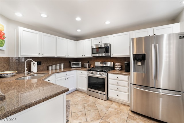 kitchen featuring sink, stainless steel appliances, tasteful backsplash, white cabinets, and dark stone counters