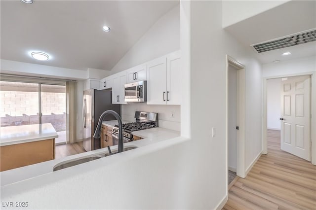 kitchen featuring lofted ceiling, sink, white cabinetry, stainless steel appliances, and light wood-type flooring