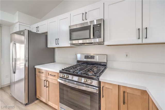 kitchen featuring lofted ceiling, appliances with stainless steel finishes, light hardwood / wood-style flooring, and white cabinets