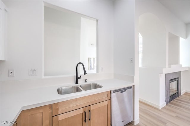 kitchen featuring a tiled fireplace, sink, stainless steel dishwasher, and light wood-type flooring