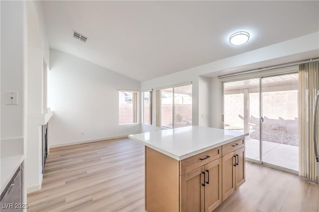 kitchen featuring lofted ceiling, light hardwood / wood-style floors, a kitchen island, light brown cabinetry, and stainless steel dishwasher