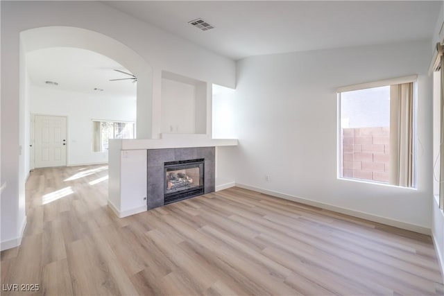 unfurnished living room with ceiling fan, a tile fireplace, and light wood-type flooring