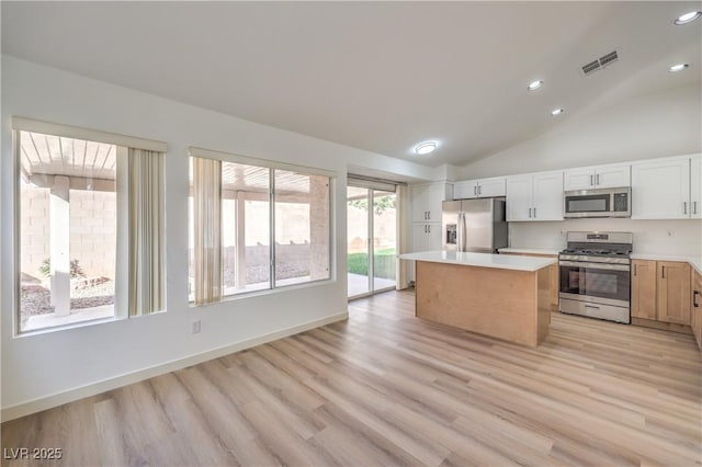 kitchen featuring appliances with stainless steel finishes, lofted ceiling, white cabinets, a center island, and light hardwood / wood-style flooring