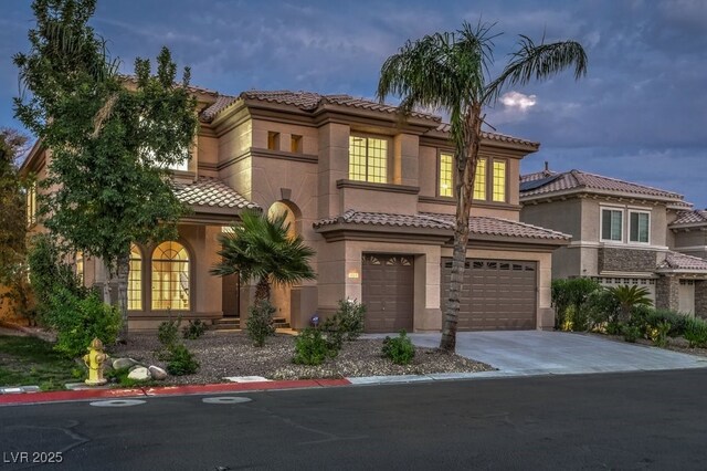 mediterranean / spanish-style home with concrete driveway, a garage, stucco siding, and a tiled roof