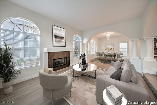 living area featuring baseboards, arched walkways, wood finished floors, and a glass covered fireplace