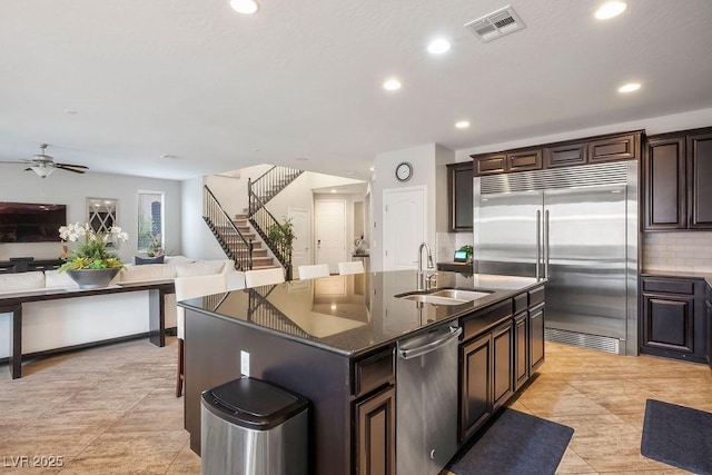 kitchen featuring dark brown cabinetry, sink, a center island with sink, appliances with stainless steel finishes, and backsplash