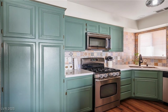 kitchen featuring sink, dark wood-type flooring, green cabinets, appliances with stainless steel finishes, and backsplash