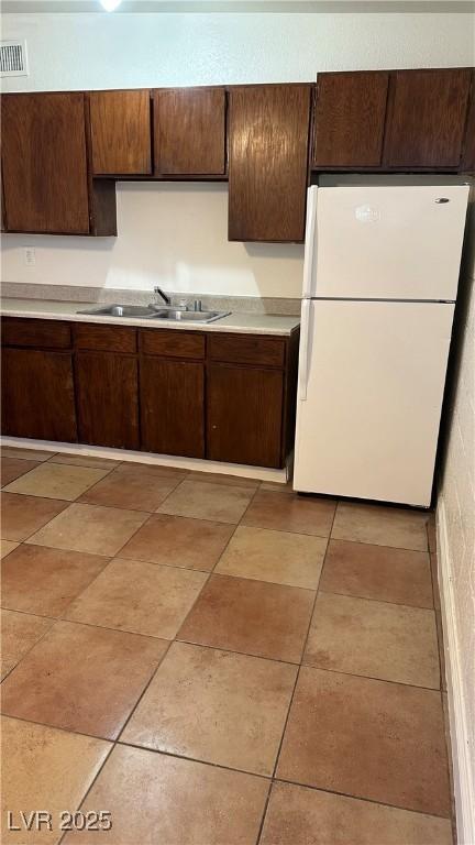 kitchen featuring dark brown cabinetry, sink, light tile patterned floors, and white refrigerator