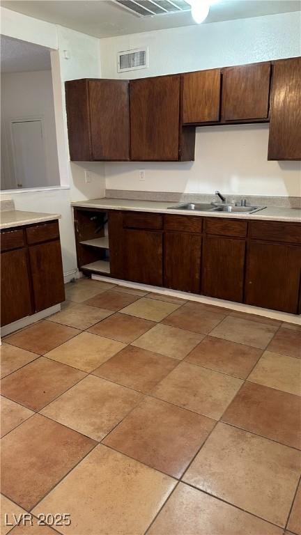 kitchen with dark brown cabinetry, sink, and light tile patterned floors