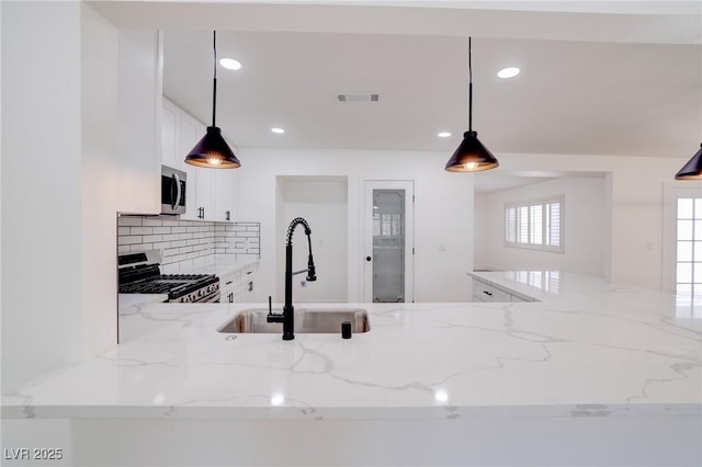 kitchen with sink, stainless steel appliances, light stone counters, tasteful backsplash, and decorative light fixtures