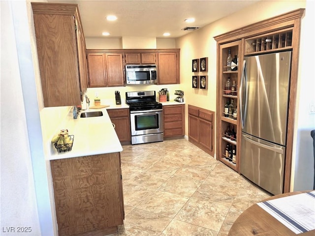 kitchen with light countertops, appliances with stainless steel finishes, brown cabinetry, and a sink