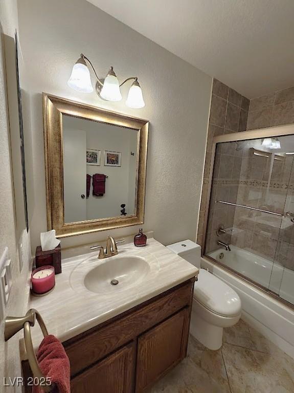 bathroom featuring toilet, a textured wall, shower / bath combination with glass door, and vanity