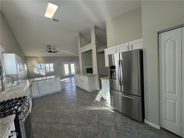 kitchen featuring lofted ceiling, sink, appliances with stainless steel finishes, light stone countertops, and white cabinets