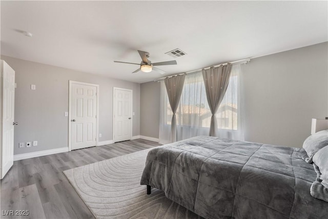 bedroom featuring ceiling fan, wood-type flooring, and two closets