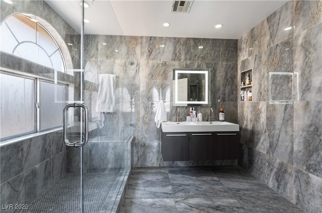 bathroom with vanity, a shower with door, and tile walls