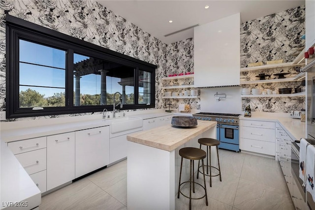 kitchen featuring wooden counters, open shelves, wallpapered walls, range with two ovens, and a sink