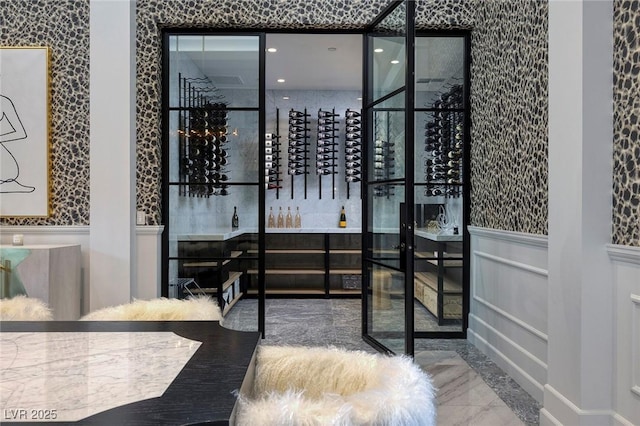 wine room featuring a decorative wall, marble finish floor, and wainscoting