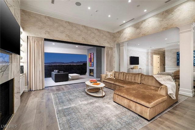 living room with ornamental molding, wood finished floors, recessed lighting, a premium fireplace, and ornate columns