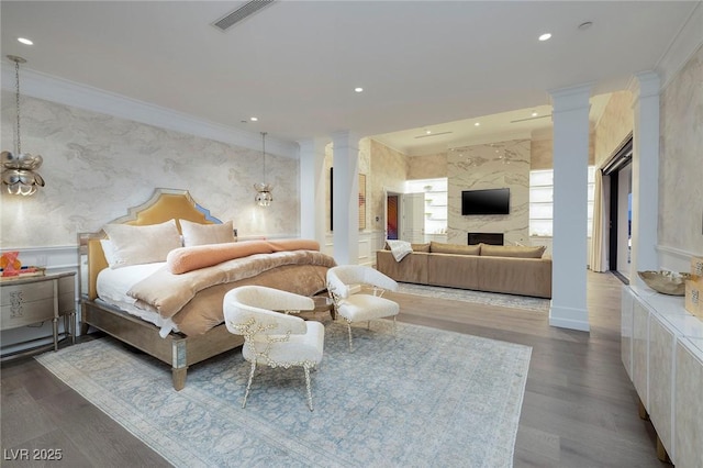 bedroom with wallpapered walls, a premium fireplace, ornamental molding, decorative columns, and wood finished floors