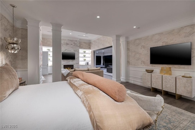 bedroom featuring wood finished floors, a premium fireplace, wainscoting, crown molding, and decorative columns