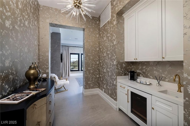 kitchen featuring wallpapered walls, baseboards, a chandelier, wine cooler, and a sink