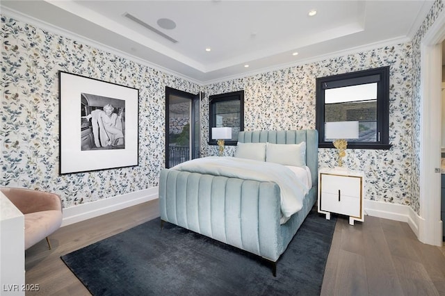 bedroom featuring a tray ceiling, wood finished floors, crown molding, wallpapered walls, and baseboards