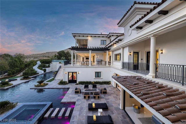 view of patio / terrace with an infinity pool, outdoor dining space, a balcony, an in ground hot tub, and stairs