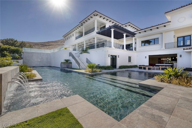 rear view of property featuring stairway, a balcony, a fenced in pool, stucco siding, and a patio area