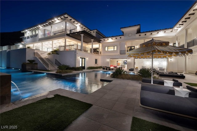 pool at night with a patio area, an outdoor pool, outdoor lounge area, and stairs