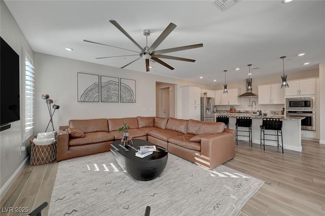 living room with sink, light hardwood / wood-style floors, and ceiling fan