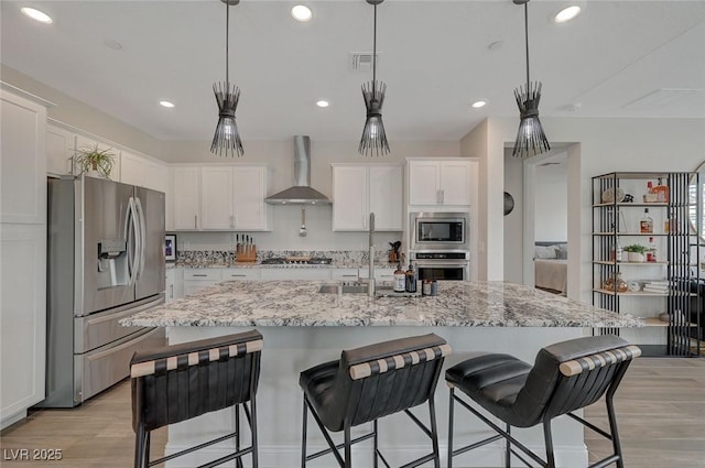 kitchen with pendant lighting, wall chimney range hood, stainless steel appliances, and white cabinets