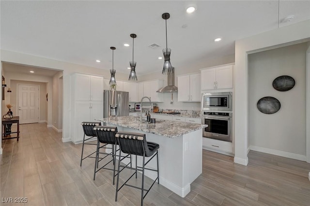 kitchen featuring white cabinetry, pendant lighting, stainless steel appliances, light stone countertops, and a kitchen island with sink