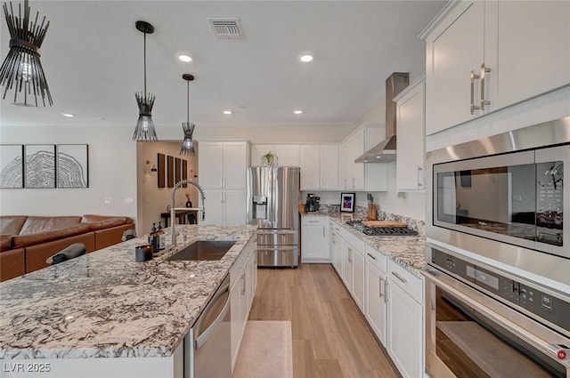 kitchen with sink, light hardwood / wood-style flooring, appliances with stainless steel finishes, white cabinetry, and a center island with sink