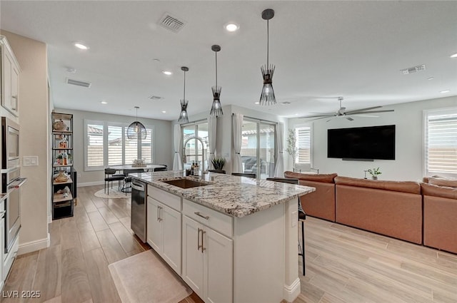 kitchen featuring sink, light stone countertops, white cabinets, and a center island with sink