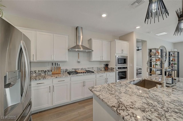 kitchen featuring stainless steel appliances, white cabinetry, wall chimney range hood, and light stone counters